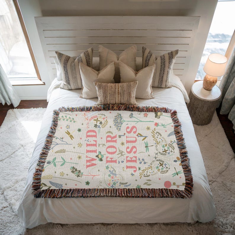 May include: A white woven throw blanket with a floral pattern and the text "WILD FOR JESUS" in pink lettering.