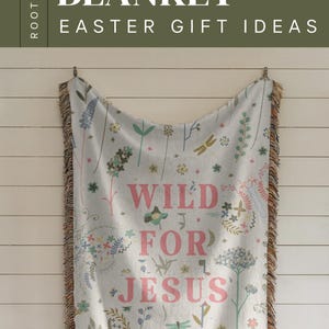 May include: A woven throw blanket with a floral pattern and the text "Wild for Jesus" in pink. The blanket has a fringe border and is hanging on a white wall.