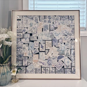 Puede incluir: Una pieza de arte mural cuadrada enmarcada que presenta un collage de numerosos sellos postales azules y blancos. Los sellos muestran varias ilustraciones, incluyendo globos terr&aacute;queos, sillas y motivos arquitect&oacute;nicos. La obra est&aacute; en un marco met&aacute;lico.