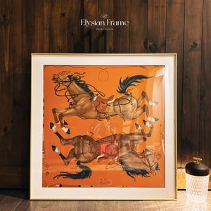 Puede incluir: Una impresi&oacute;n cuadrada enmarcada con fondo naranja que muestra dos caballos marrones en una composici&oacute;n espejada. Los caballos est&aacute;n representados con sillas de montar, bridas y riendas. El texto Elysian Frame Elevate the Icon es visible sobre el marco.