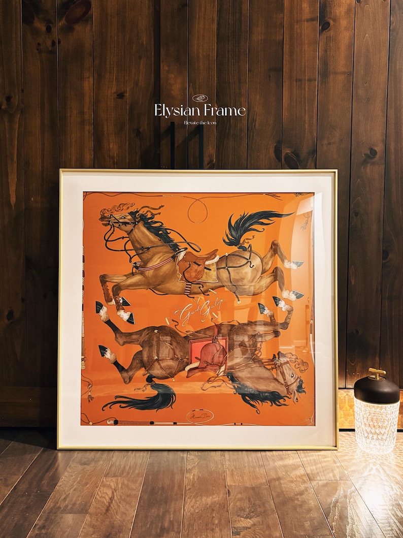 Puede incluir: Una impresi&oacute;n cuadrada enmarcada con fondo naranja que muestra dos caballos marrones en una composici&oacute;n espejada. Los caballos est&aacute;n representados con sillas de montar, bridas y riendas. El texto Elysian Frame Elevate the Icon es visible sobre el marco.