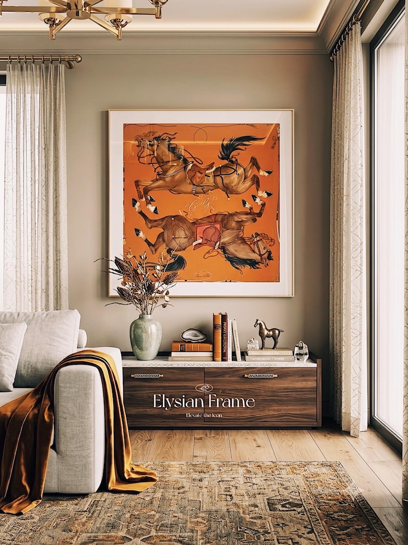 Puede incluir: Una pieza de arte mural cuadrada enmarcada que presenta un fondo naranja con dos caballos marrones con arn&eacute;s, exhibida sobre una mesa consola de madera con el texto Elysian Frame Elevate the Icon impreso en el panel del caj&oacute;n frontal.