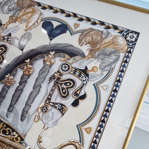 Puede incluir: Una l&aacute;mina enmarcada que muestra un caballo blanco con crines trenzadas, adornado con elementos decorativos de arn&eacute;s en dorado, negro y azul, plumas y detalles en forma de coraz&oacute;n. La obra est&aacute; dentro de un marco dorado fino con un paspart&uacute; blanco.