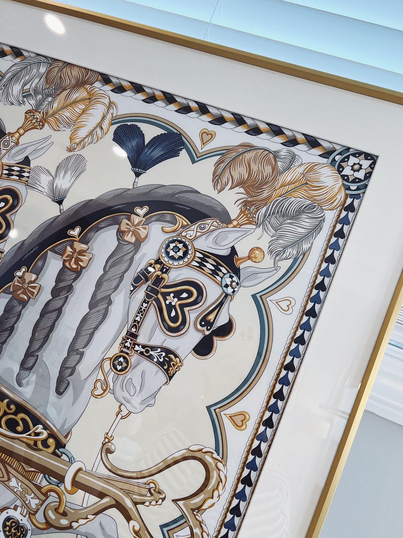 Puede incluir: Una l&aacute;mina enmarcada que muestra un caballo blanco con crines trenzadas, adornado con elementos decorativos de arn&eacute;s en dorado, negro y azul, plumas y detalles en forma de coraz&oacute;n. La obra est&aacute; dentro de un marco dorado fino con un paspart&uacute; blanco.