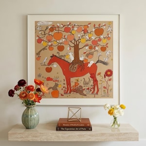 Puede incluir: Una impresi&oacute;n cuadrada enmarcada que muestra un caballo rojo con un &aacute;rbol creciendo en su lomo, cargado de manzanas naranjas y amarillas. La escena incluye peque&ntilde;os conejos blancos, ardillas y p&aacute;jaros sobre un fondo beige con el texto "de Pomme en Soline".