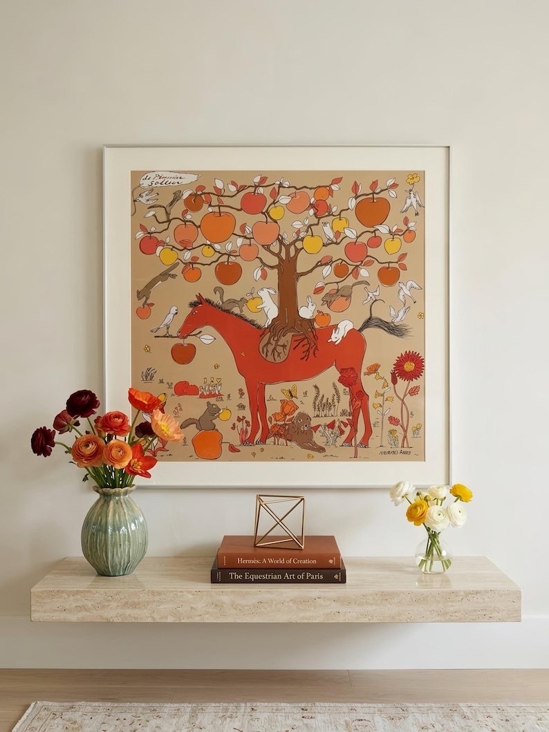 Puede incluir: Una impresi&oacute;n cuadrada enmarcada que muestra un caballo rojo con un &aacute;rbol creciendo en su lomo, cargado de manzanas naranjas y amarillas. La escena incluye peque&ntilde;os conejos blancos, ardillas y p&aacute;jaros sobre un fondo beige con el texto "de Pomme en Soline".