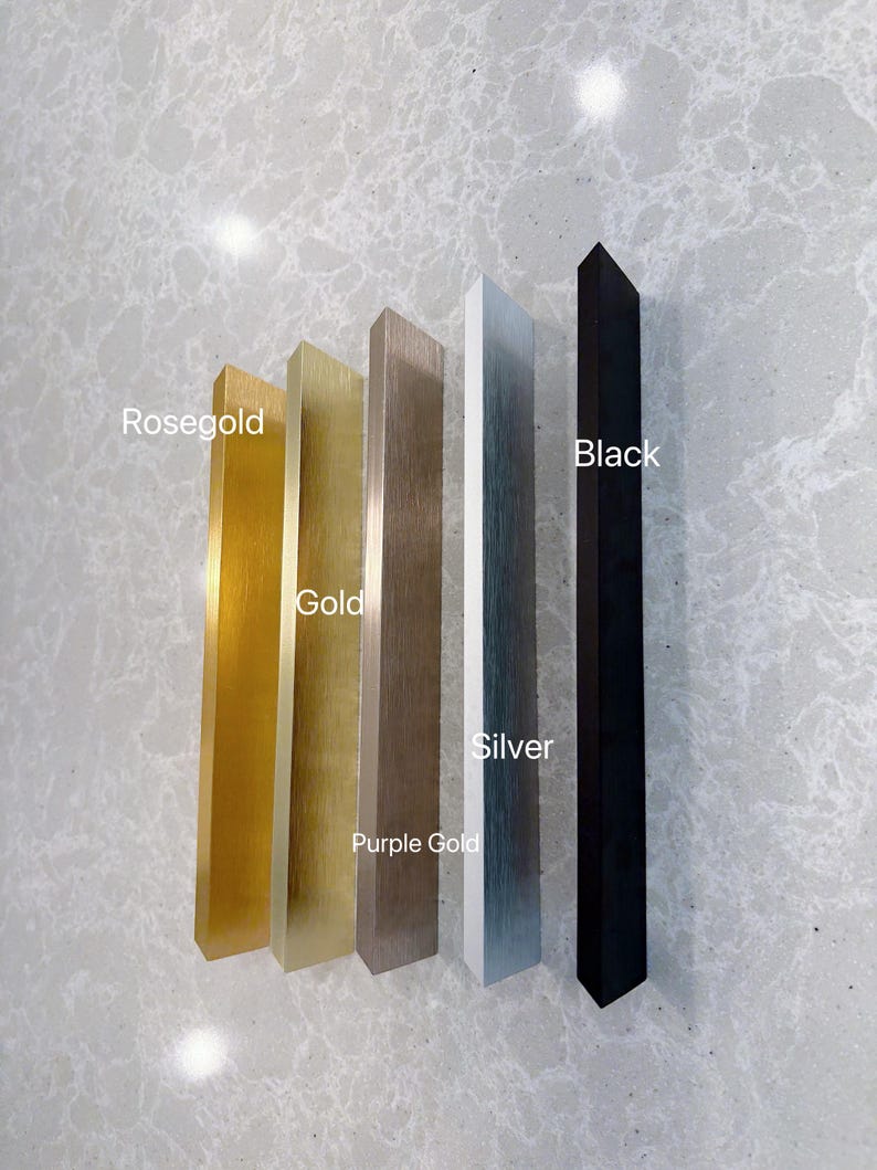 Puede incluir: Cinco tiradores de armario rectangulares dispuestos verticalmente. Los acabados de izquierda a derecha est&aacute;n etiquetados como Rosegold, Gold, Purple Gold, Silver y Black. Cada tirador tiene una textura met&aacute;lica cepillada, excepto el negro mate.