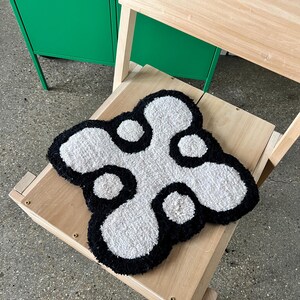 May include: A white and black fluffy rug with a unique abstract design. The rug is placed on a wooden chair.
