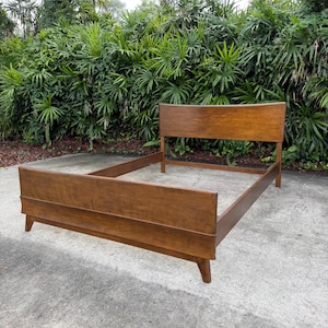 May include: A medium-brown wooden bed frame featuring a tall, rectangular headboard and a lower footboard. The frame is constructed with clean, straight lines and is supported by four tapered legs, showcasing a smooth, polished wood grain finish.