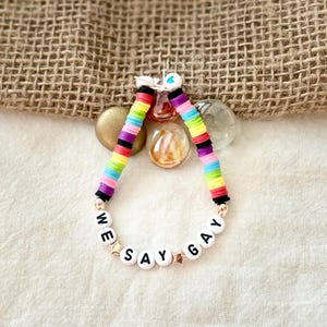 May include: A rainbow-colored beaded bracelet with the words "We Say Gay" spelled out in black letters on white beads.