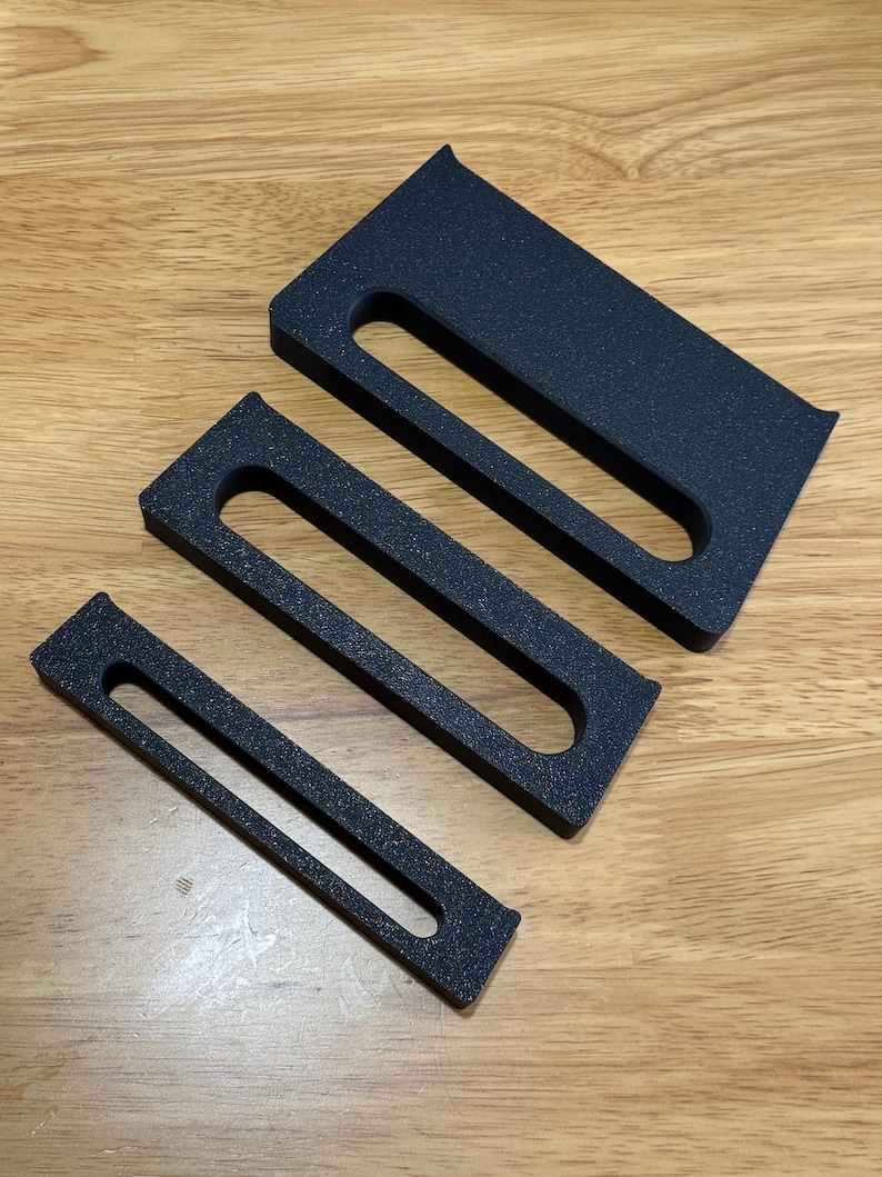 May include: Three black foam inserts of different sizes with a rectangular shape and a cutout in the middle. The inserts are designed to fit inside a box or container.