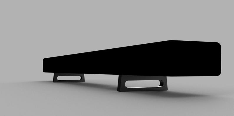 May include: A black sound bar with two black metal legs on each end. The sound bar is rectangular and has a sleek, modern design.