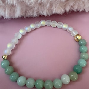 Könnte beinhalten: Ein Armband aus grünen und weißen Perlen. Die Perlen sind in der Größe abgestuft, wobei die größeren Perlen grün und die kleineren Perlen weiß sind. Das Armband ist mit goldenen Perlen verziert.