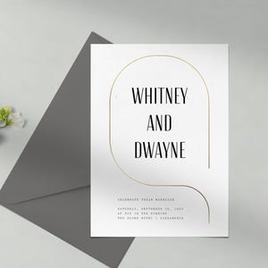 May include: A white wedding invitation with gold foil accents. The invitation features the names "Whitney and Dwayne" and details about their wedding celebration. The invitation is on a gray background.
