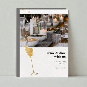 May include: A white card with a gold champagne flute illustration and the text "wine & dine with us" in black. The card also includes the date "MAY 22ND, 1887", the time "AT 7 P.M." and the location "HOLMES MANOR". The background of the card is a blurry image of a table setting with candles and glasses.