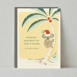 May include: A Christmas greeting card featuring a koala in a Santa hat on a palm tree. The card has a yellow background with the text "Sending our best to you & yours". A small sailboat, starfish, and seashell are also depicted.