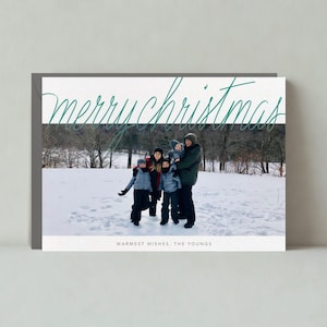 Puede incluir: Tarjeta de felicitación navideña con una foto familiar en un paisaje nevado. Las palabras "merry christmas" están escritas en verde. La parte inferior de la tarjeta dice "warmest wishes, the Youngs."