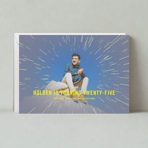 May include: A birthday card with a blue and yellow color scheme. The card features a photo of a person sitting on a rock with a blue sky and white streaks of light in the background. The text on the card reads "Holden is turning twenty-five".