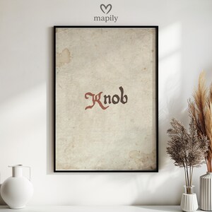 May include: Framed art print with the word "Knob" in a vintage font. The text is dark red on a textured, aged paper background with brown stains. The print is in a black frame. The print has a vintage aesthetic.