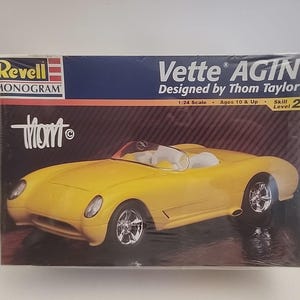 May include: A yellow Revell Monogram model car kit of a Vette AGIN, designed by Thom Taylor. The box shows a yellow convertible car with chrome wheels. The kit is 1:24 scale and for ages 10 & up.
