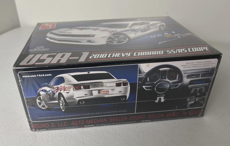 Puede incluir: Caja de modelo de un Chevy Camaro SS/RS Coupe de 2010. La caja presenta im&aacute;genes del coche blanco con gr&aacute;ficos con tem&aacute;tica de la bandera estadounidense. El texto "USA-1" es visible.