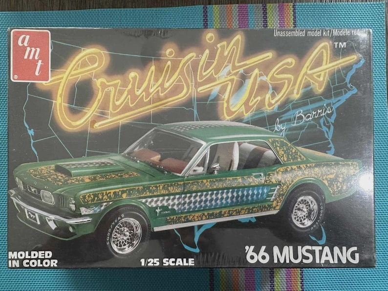 Puede incluir: Caja de modelo de un coche Mustang '66 verde con detalles dorados y a cuadros. La caja tiene el texto "Cruisin' USA" en una fuente de estilo ne&oacute;n, y "1/25 Scale" est&aacute; impreso en la caja.
