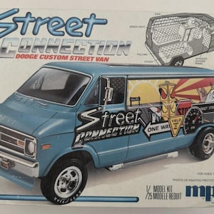 May include: A model kit box for a Dodge Custom Street Van. The box features a blue van with custom graphics, including a street scene with a traffic light and the text "Street Connection." Includes a diagram of the van's interior. For ages 10 to adult.