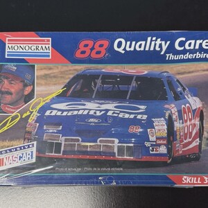 May include: A model kit box featuring a blue and red race car with the number 88 and the words "Quality Care" and "Thunderbird." The box includes a picture of a man and the text "NASCAR."