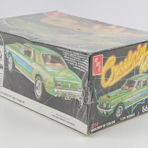 Puede incluir: Caja de kit de modelo de coche vintage con un Mustang '66 verde y azul. La caja tiene las palabras "Cruisin' USA" en amarillo y el texto "Molded in Color". La caja es a escala 1/25 y es para mayores de 10 a&ntilde;os.