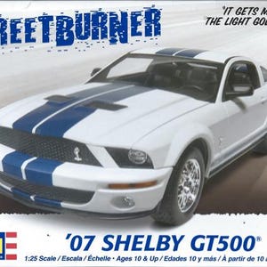 May include: A white 1:25 scale model kit of a 2007 Ford Shelby GT500 Mustang with blue racing stripes. The box features the text "Streetburner" and "It gets mean when the light goes green!"