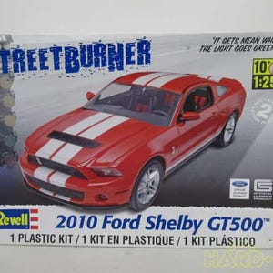 May include: A Revell model kit of a red 2010 Ford Shelby GT500 with white racing stripes. The box features the text "STREETBURNER" and "IT GETS MEAN WHEN THE LIGHT GOES GREEN!" The model is 1:25 scale.