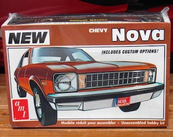 Puede incluir: Una caja de cartón rectangular para un kit de modelo de coche AMT Chevy Nova. La caja presenta un diseño en marrón y blanco con una ilustración de un Chevy Nova naranja, el texto NEW, CHEVY Nova e INCLUDES CUSTOM OPTIONS! en negro y blanco.