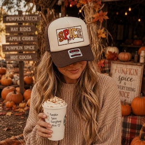 Puede incluir: Una gorra de camionero marrón y crema con un parche rectangular que muestra el texto "SPICE girl" en letras naranjas y marrones. La gorra tiene una parte trasera de malla y un panel frontal sólido. Se sostiene un vaso blanco con el texto "Pumpkin Spice Everything Nice".