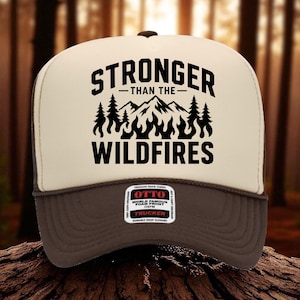 May include: A cream and brown trucker hat featuring a black graphic print of mountains, pine trees, and flames with the text STRONGER THAN THE WILDFIRES. A rectangular sticker on the brim displays the brand name OTTO and product details.