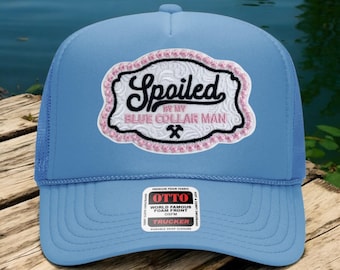 Può includere: Cappellino da camionista azzurro con una toppa ricamata bianca e rosa con la scritta "Spoiled by my Blue Collar Man". Il cappello ha un retro in rete e una visiera curva. Una piccola etichetta bianca recita "OTTO".