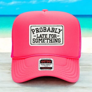 May include: A bright pink trucker hat with a mesh back and a curved brim. The front features a rectangular patch with the words "PROBABLY - LATE FOR - SOMETHING" in black lettering. The hat has a snap closure.