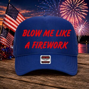Puede incluir: Una gorra de camionero azul real con el texto rojo BLOW ME LIKE A FIREWORK impreso en el panel frontal de espuma. La gorra incluye una pequeña pegatina rectangular blanca con texto negro que dice OTTO WORLD FAMOUS FOAM FRONT OSFN TRUCKER.