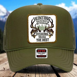 May include: An olive green trucker hat with a mesh back and foam front. The front patch reads "HUNTING SOLVES MOST OF MY PROBLEMS FISHING SOLVES THE REST" with deer antlers and fish illustrations. A small Otto patch is on the front.