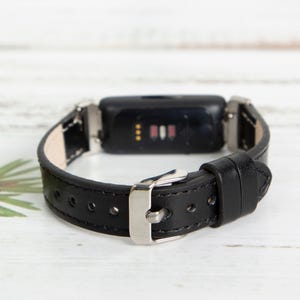 May include: Black leather watch band with a silver buckle and a black fitness tracker with a silver trim.