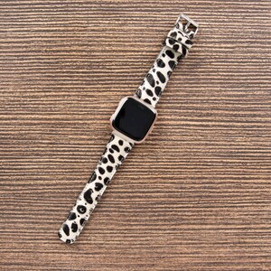 May include: A smartwatch with a black screen and a white and black spotted band. The watch has a silver-colored frame and a silver buckle. The band is made of a material with a pattern of black spots on a white background.