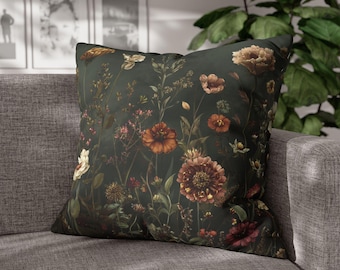 Op de afbeelding: Vierkant sierkussen met een bloemenpatroon op een donkergroene achtergrond. De bloemen zijn in tinten oranje, bruin en crème. Het kussen ligt op een grijze bank.