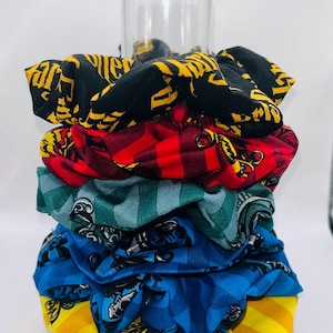 May include: A stack of six colorful hair scrunchies with a Harry Potter theme. The scrunchies feature different patterns and colors, including black, yellow, red, green, and blue. The scrunchies are made of fabric and have a soft, comfortable feel.