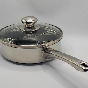 Puede incluir: Una poachadora de huevos de acero inoxidable con tapa de cristal y asa. La poachadora tiene cuatro tazas individuales para escalfar huevos. La tapa tiene un pomo plateado. El asa es curva y tiene un agujero en el extremo.