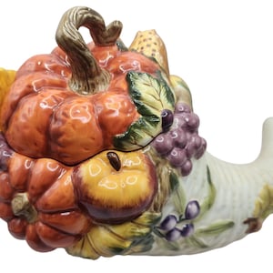Puede incluir: Un plato de servir de cerámica con forma de cuerno de la abundancia decorado con una variedad de frutas y verduras de otoño, incluyendo una calabaza, uvas, manzanas y calabazas.