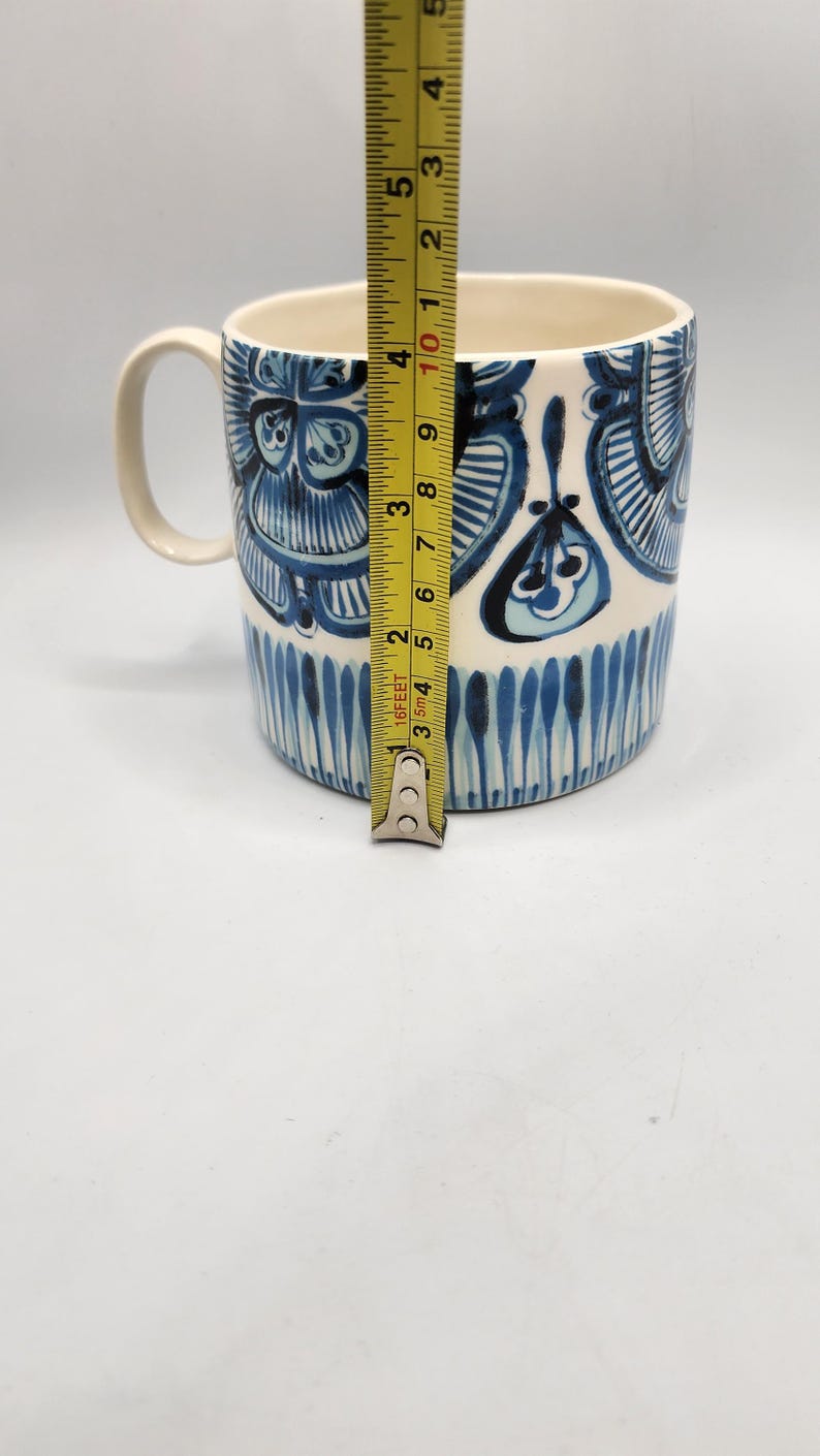 May include: A ceramic mug with a white interior and a blue and white floral design. The mug is approximately 4 inches tall. The handle is white. The mug is on a white background.