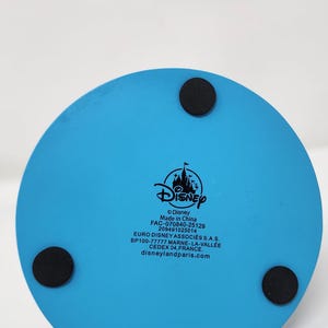 Pu&ograve; includere: Una base rotonda blu chiaro con marchio Disney con tre piedini circolari neri. Il logo Disney e il testo sono stampati sulla base. Il testo include "Made in China" e "disneylandparis.com".