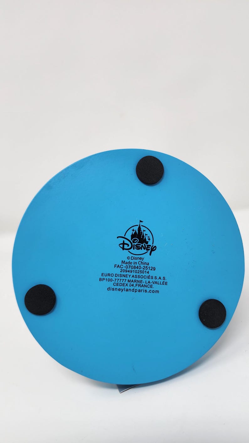 Pu&ograve; includere: Una base rotonda blu chiaro con marchio Disney con tre piedini circolari neri. Il logo Disney e il testo sono stampati sulla base. Il testo include "Made in China" e "disneylandparis.com".