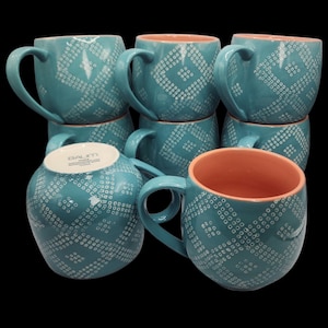 May include: A stack of teal ceramic mugs with a white geometric pattern. The interior of each mug is a peach color. Each mug has a large handle for easy gripping. The mugs are stacked on top of each other.