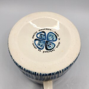 May include: White stoneware mug with a blue floral design and a handle. The mug has a blue rim and the words "quality stoneware...made in china...fabriqu&eacute; en chine" printed on the bottom.
