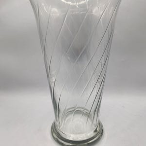 May include: Clear glass vase with a flared top and a wide, circular base. The vase features a spiral design etched into the glass, creating a textured effect. The vase is empty and sits against a plain white background.